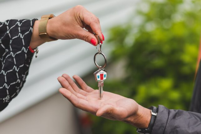 Hand overhandigt huissleutel met huisvormige sleutelhanger
